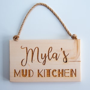 Peut inclure: Une pancarte en bois avec une suspension en corde, indiquant "Myla's Mud Kitchen".