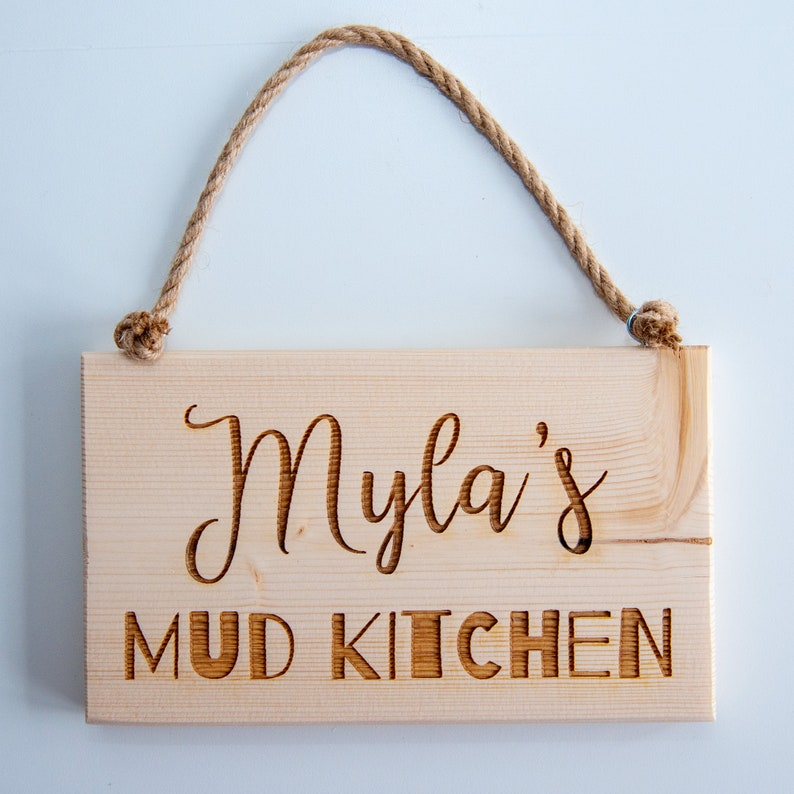 Peut inclure: Une pancarte en bois avec une suspension en corde, indiquant "Myla's Mud Kitchen".