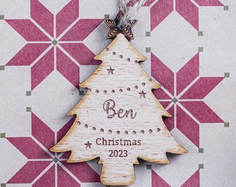 Könnte beinhalten: Weihnachtsbaumschmuck aus Holz in Form eines Baumes, mit dem Namen "Ben" und dem Text "Christmas 2023" eingraviert. Der Schmuck hat Stern- und Punktdetails und einen Stern oben. Er hängt an einer natürlichen Schnur.