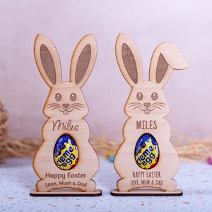 Personalised Easter Egg Holder made from 3mm wood or 4mm Beech Veneered Wood, Egg holder has a cut out to fit Kinder Surprise Egg and Cadbury Egg Creme, Name engraved in front of the wooden Easter bunny standing with a base.