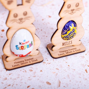 Personalised Easter Egg Holder made from 3mm wood or 4mm Beech Veneered Wood, Egg holder has a cut out to fit Kinder Surprise Egg and Cadbury Egg Creme, Name engraved in front of the wooden Easter bunny standing with a base.