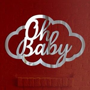 Może przedstawiać: Srebrny, lustrzany znak w kształcie chmury z napisem "Oh Baby" w ozdobnym, pochylonym piśmie.