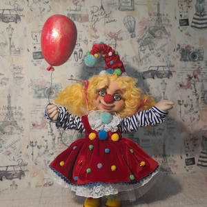 May include: A handmade clown doll with blonde hair, a red and white striped shirt, a red velvet dress with colorful polka dots, and a blue and white hat. The doll is holding a red balloon.