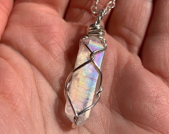 May include: A silver necklace featuring a clear, iridescent crystal pendant. The crystal is wrapped in silver wire and hangs from a delicate chain. The crystal displays a rainbow of colors.