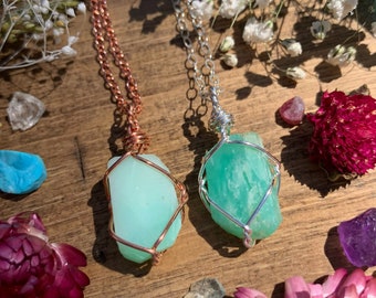May include: Two necklaces with green gemstone pendants wrapped in wire. One necklace has a copper chain and the other has a silver chain.