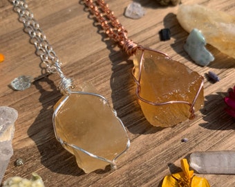 May include: Two necklaces with raw, golden citrine crystal pendants wrapped in wire. One necklace has a silver chain and the other has a copper chain.