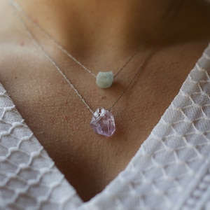 May include: A silver chain necklace with two crystal pendants. The top pendant is a light blue aquamarine, and the bottom pendant is a purple amethyst.