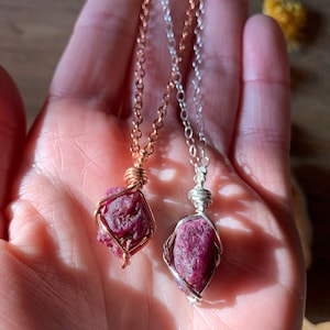 May include: Two ruby gemstone pendants, one wrapped in copper wire and the other in silver wire, hanging from delicate chains.