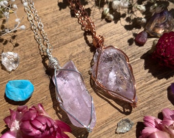 May include: Two necklaces with pink crystal pendants wrapped in wire. One necklace has a silver chain and the other has a copper chain.