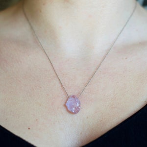 May include: A silver chain necklace with a light pink, irregularly shaped crystal pendant.