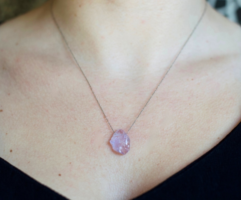 May include: A silver chain necklace with a light pink, irregularly shaped crystal pendant.