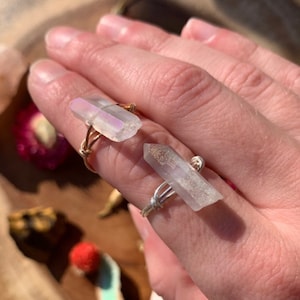 Puede incluir: Dos anillos con cristales de cuarzo transparentes envueltos en alambre dorado. Los cristales son iridiscentes y tienen una apariencia ligeramente nublada.