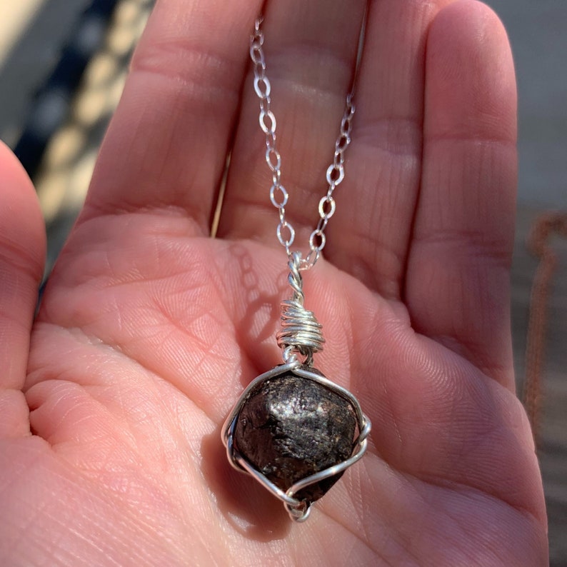 May include: A silver chain necklace with a dark gray, faceted gemstone pendant wrapped in silver wire.