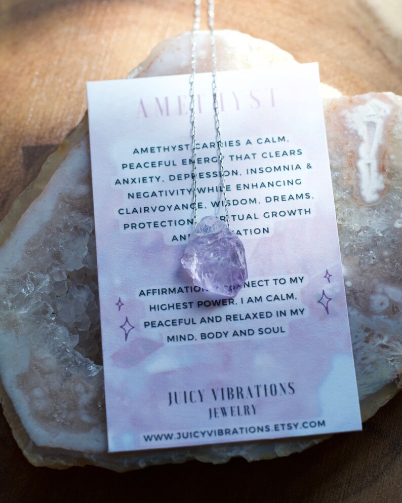 May include: Amethyst crystal necklace with a silver chain. The necklace is displayed on a white card with text about the healing properties of amethyst. The text reads: "Amethyst carries a calm, peaceful energy that clears anxiety, depression, insomnia & negativity while enhancing clairvoyance, wisdom, dreams, protection and spiritual growth and affirmation. Connect to my highest power. I am calm, peaceful and relaxed in my mind, body and soul. Juicy Vibrations Jewellery www.juicyvibrations.etsy.com"
