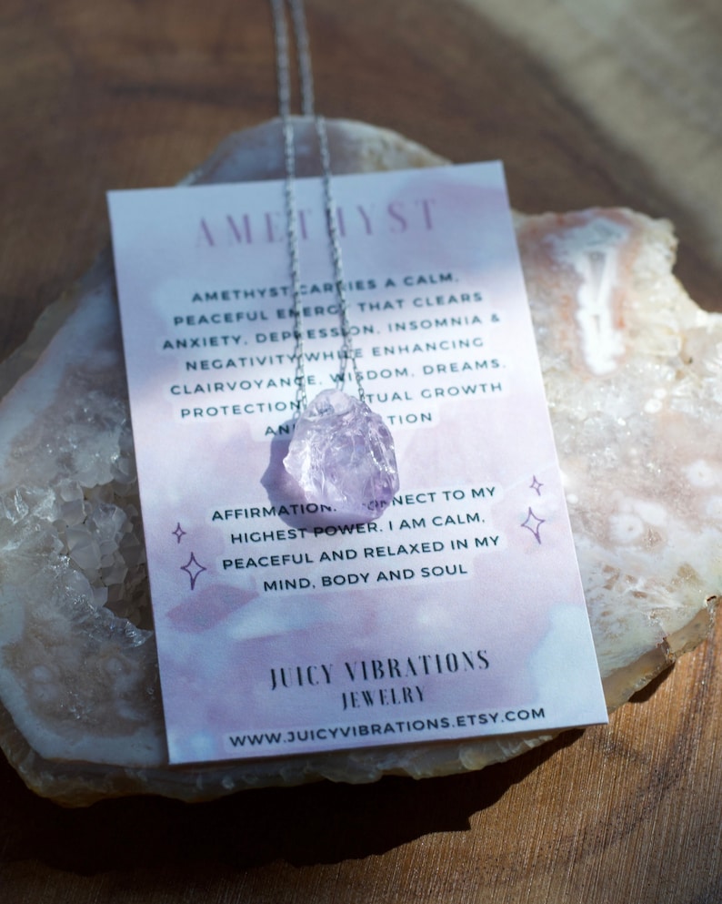 May include: Amethyst crystal necklace with a silver chain. The card reads "Amethyst carries a calm, peaceful energy that clears anxiety, depression, insomnia & negativity while enhancing clairvoyance, wisdom, dreams, protection and spiritual growth. Affirmation: I connect to my highest power. I am calm, peaceful and relaxed in my mind, body and soul. Juicy Vibrations Jewellery www.juicyvibrations.etsy.com"