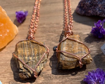 May include: Two gold tiger's eye stone pendants wrapped in copper wire on a copper chain necklace. The stones are raw and have a natural, rough texture.