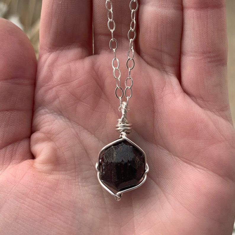 May include: A silver chain necklace with a dark red gemstone pendant wrapped in silver wire.