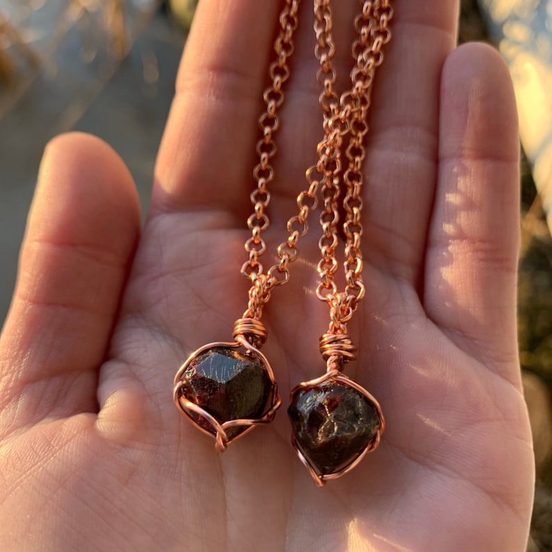 May include: Two copper wire wrapped garnet pendants on copper chains. The garnets are dark red and have a faceted, geometric shape.