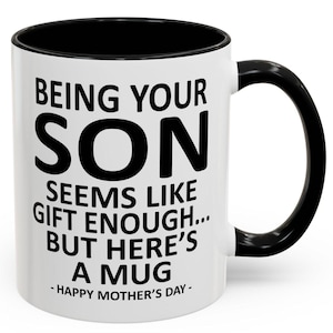 May include: White ceramic mug with a black interior and handle. The mug features the text "BEING YOUR SON SEEMS LIKE GIFT ENOUGH... BUT HERE'S A MUG - HAPPY MOTHER'S DAY-" in black lettering.