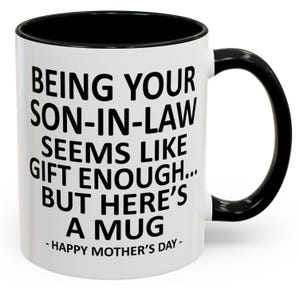 May include: White ceramic mug with a black interior, handle, and rim. The mug features the text "BEING YOUR SON-IN-LAW SEEMS LIKE GIFT ENOUGH... BUT HERE'S A MUG - HAPPY MOTHER'S DAY-" in black lettering.
