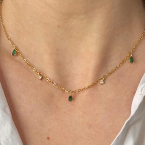 Op de afbeelding: Een gouden ketting met kleine groene en heldere edelsteen accenten.