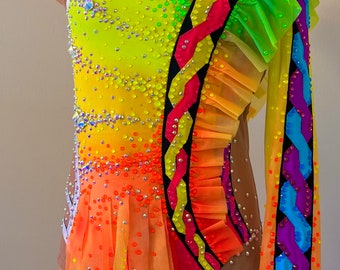 May include: A colorful leotard with a rainbow ombre design and a large flower accent on the shoulder. The leotard is decorated with rhinestones and has a black and white trim.