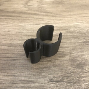 May include: A black 3D-printed object with a unique shape, featuring two curved sections connected by a smaller, circular element. The object is made of a solid, matte black material and sits on a wooden surface.