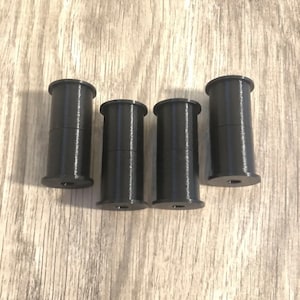 May include: Four black plastic spools, each with a small hole in the center.
