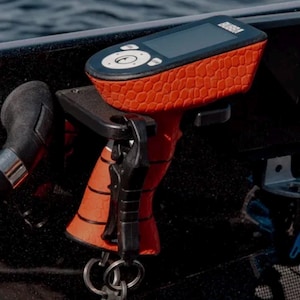May include: A red and black fish finder with a textured grip and a digital display. The device is mounted on a black surface.