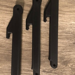 May include: Three black plastic parts with a small hole at the top and a cut-out on the side. The parts are similar in shape and size.