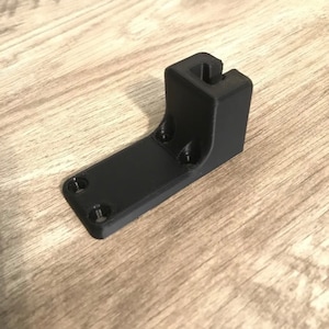 May include: A black plastic 3D printed wall mount with a slot for a device.