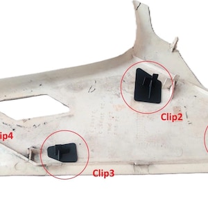May include: A light beige car interior trim panel with four black clips attached. The panel has a curved shape with a rectangular opening and various mounting points. The clips are labeled Clip1, Clip2, Clip3, and Clip4.
