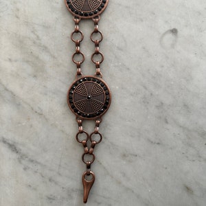 May include: A copper chain belt with two round black and copper medallions. Each medallion has a cross design with black rhinestones.
