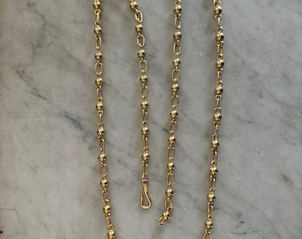May include: A gold chain necklace with round beads. The chain is made of small, linked circles with a round bead at each link.