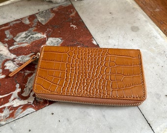 May include: A brown leather wallet with a crocodile embossed pattern and a zipper closure.