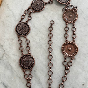 May include: A copper chain belt with five round, decorative medallions. The medallions have a black rhinestone design and a textured surface.