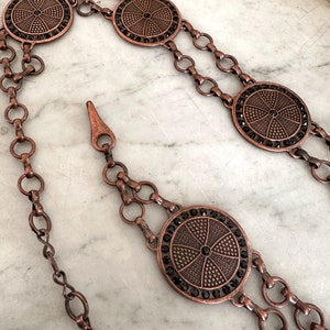 May include: A copper chain belt with four round, decorative, black rhinestone-encrusted medallions.