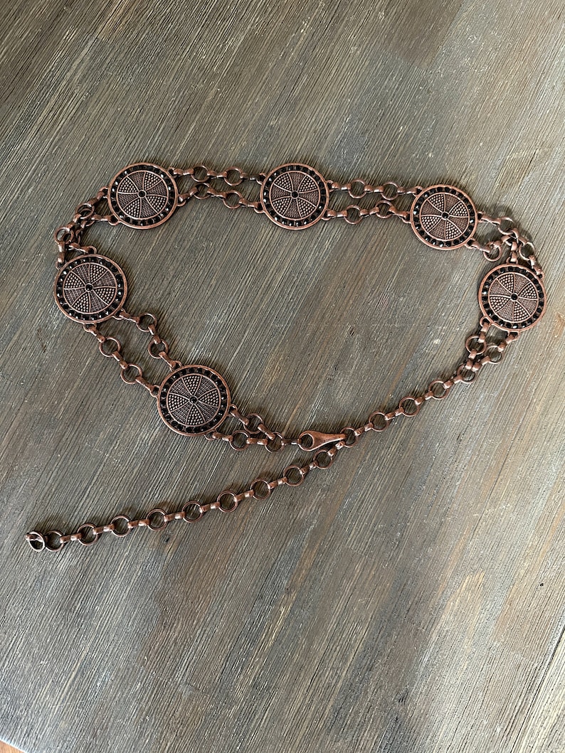 May include: A copper chain belt with circular metal accents. The accents have a black, geometric design.