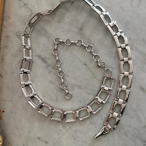Peut inclure: Un collier en chaîne argentée avec un motif de maillons carrés. Le collier a une petite chaîne d'extension.
