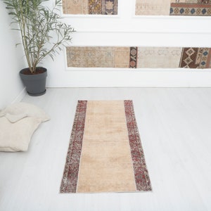 May include: A beige runner rug with a red and brown patterned border. The rug is on a white floor.