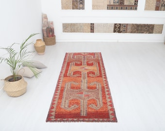 May include: A long, narrow red and orange runner rug with a geometric pattern. The rug has a fringe on both ends.