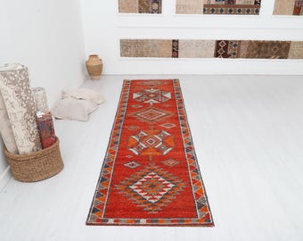 May include: A red, orange, and gray patterned runner rug with a geometric design. The rug is laid out on a white floor.