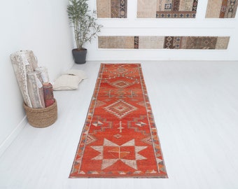 May include: A long, red runner rug with a geometric pattern in shades of orange, brown, and white. The rug has a traditional, tribal design.