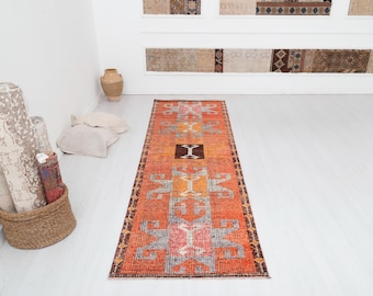 May include: A long, narrow rug with a traditional Turkish design. The rug has a red, orange, and brown color scheme with intricate geometric patterns.