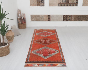 May include: A red, orange, and gray patterned runner rug with a geometric design. The rug has a fringe border.
