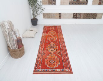 May include: A red, orange, and blue patterned runner rug with a geometric design. The rug is laid out on a white floor.