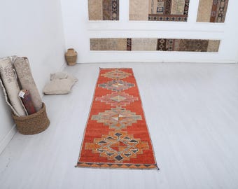 Könnte beinhalten: Ein orangefarbener Läufer mit geometrischen Mustern in Beige, Braun und Blau. Der rechteckige Teppich hat ein zentrales Design mit sich wiederholenden Diamant- und Rechteckformen. Er ist wahrscheinlich aus gewebtem Material.