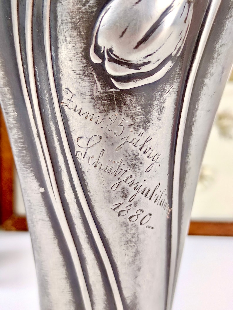 K&ouml;nnte beinhalten: Eine silberne Metallvase mit einem Tulpenmotiv und der Inschrift "Zum 25 j&auml;hrig Sch&uuml;tzenjubil&auml;um 1880".