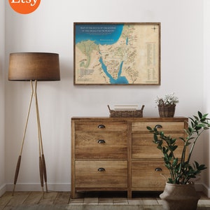 May include: A printable map of the route of the Exodus of the Israelites from Egypt. The map is printed on parchment paper and has a brown wooden frame. The map is displayed on a wall in a room with a wooden dresser, a lamp, and a potted plant.