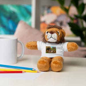 May include: A plush lion toy with a brown mane and orange fur. The lion wears a white t-shirt with a colorful graphic print. A white mug and colored pencils are in the background.